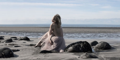 Young woman on rock by lake against sky