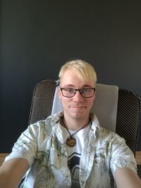 Portrait of young man wearing eyeglasses while sitting on chair at home