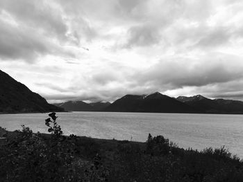 Scenic view of lake by mountains against cloudy sky