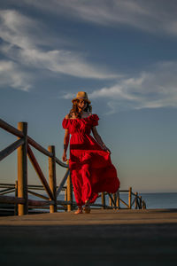 Woman standing on railing by sea against sky