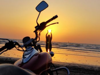 Man riding motorcycle on beach against sky during sunset