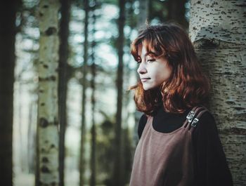Beautiful young woman looking at tree trunk in forest