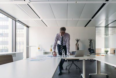 Businessman with documents standing at conference table in board room