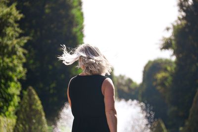 Rear view of woman with tousled hair standing against trees