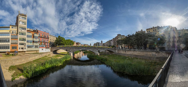 Bridge over river amidst buildings in city against sky