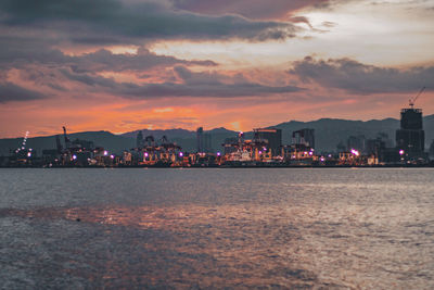 Sea by illuminated buildings against sky during sunset