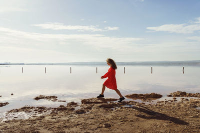 Side view of woman standing at beach against sky