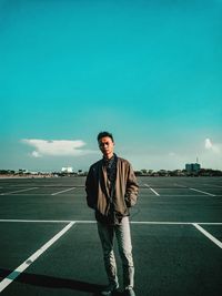 Full length portrait of young man standing on road against sky