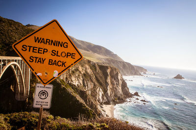 Road sign by sea against clear sky