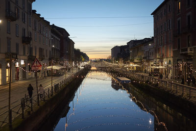 Canal amidst city buildings against sky during sunset