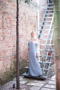 Full length of happy woman standing against brick wall