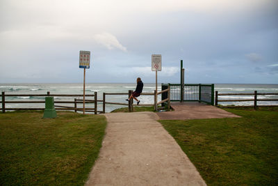 Man on railing by sea against sky