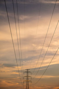 Low angle view of electricity pylon against sky at sunset