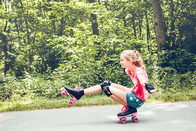 Side view of girl roller skating on road against forest