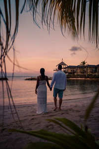 Rear view of couple standing at beach during sunset