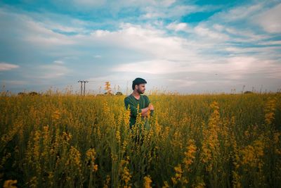 Thoughtful man standing at rape field against cloudy sky
