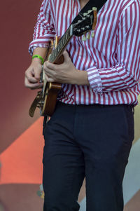 Midsection of man playing guitar against red wall