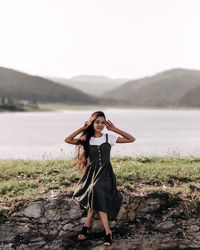 Portrait of young woman sitting on rock against lake