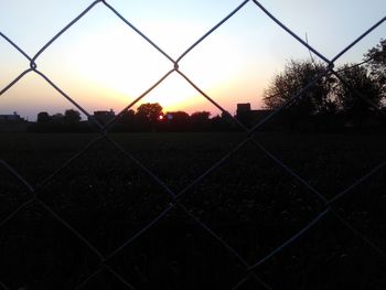 Close-up of chainlink fence against sky during sunset