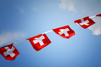 Low angle view of swiss flags hanging against sky