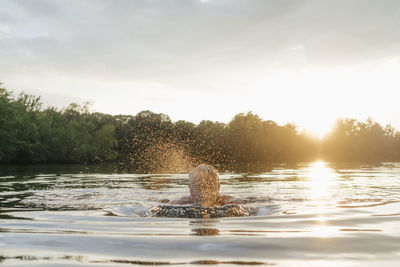 Senior man swimming in a lake at sunset