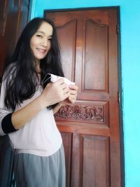 Portrait of smiling young woman standing against door