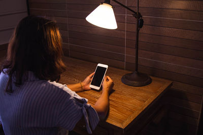 Woman using blank phone by illuminated lamp at table