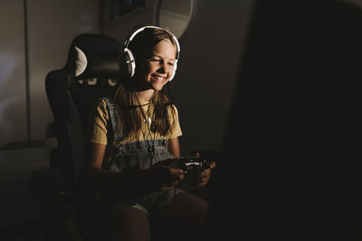 Smiling girl playing video game at home in dark
