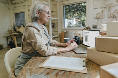 Craftswoman using laptop on workbench in workshop