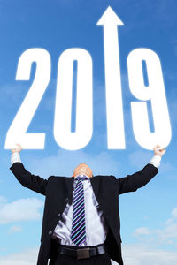 Digital composite image of businessman holding 2019 against blue sky