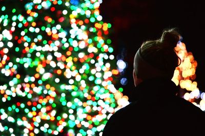 Rear view of man with illuminated christmas tree in city at night