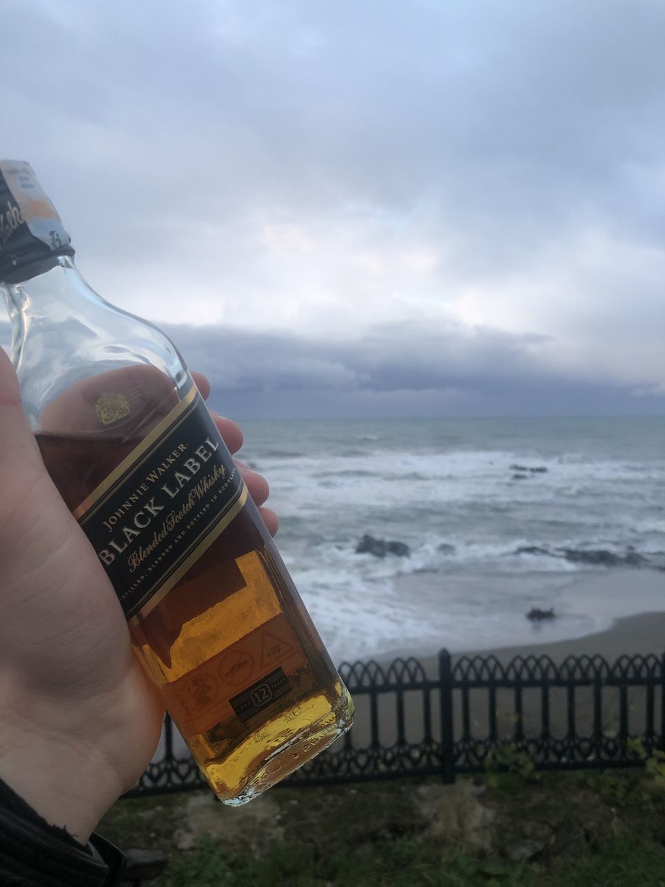 CROPPED IMAGE OF HAND HOLDING BOTTLE AGAINST SEA