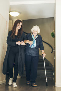 Full length of young woman assisting grandmother to walk by steps