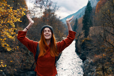 Smiling young woman with arms raised standing in autumn