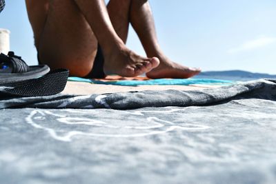 Low section of man sitting at beach against sky