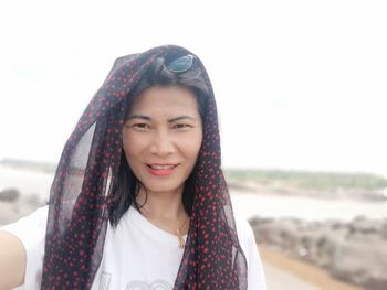 Portrait of smiling young woman on beach against sky