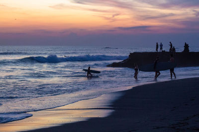 Silhouette people on beach against sky during sunset