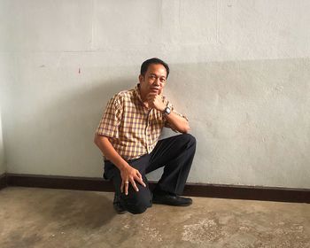 Portrait of mature man crouching against wall