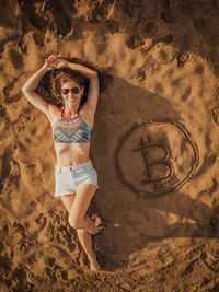 Full length of woman lying by bitcoin symbol at beach