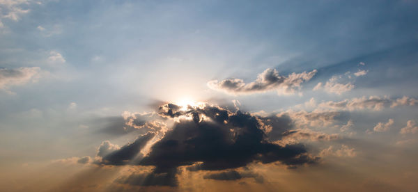 Low angle view of sunlight streaming through clouds