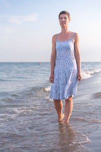 Portrait of young woman standing at beach against sky