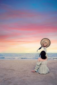 Rear view of woman sitting on beach during sunset