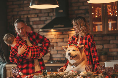 Candid authentic happy family spends time together enjoying dog with reindeer antlers at xmas lodge