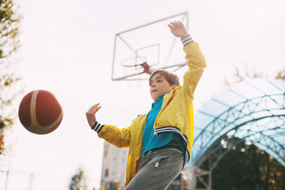 Low angle view of boy playing with ball in court