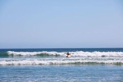 Scenic view of sea with man surfing against clear sky