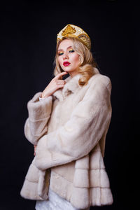 Beautiful woman wearing fur jacket and crown against black background