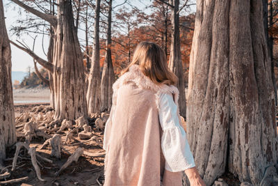 Rear view of woman standing by tree trunk in forest