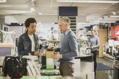 Mature salesman showing appliance to male customer in electronics store