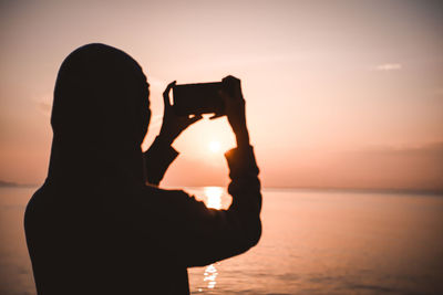 Rear view of silhouette person photographing against sky during sunset