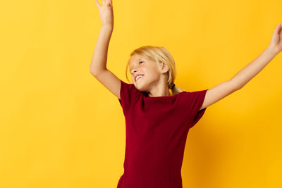 Young woman with arms raised standing against yellow background